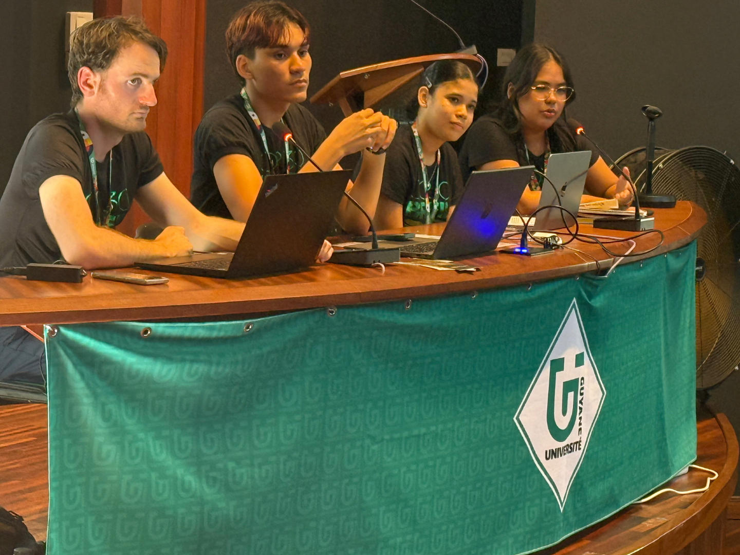 Quatre étudiants de l’Université de Guyane participent à une table ronde, assis derrière une table avec microphones et ordinateurs, lors d’un événement académique.