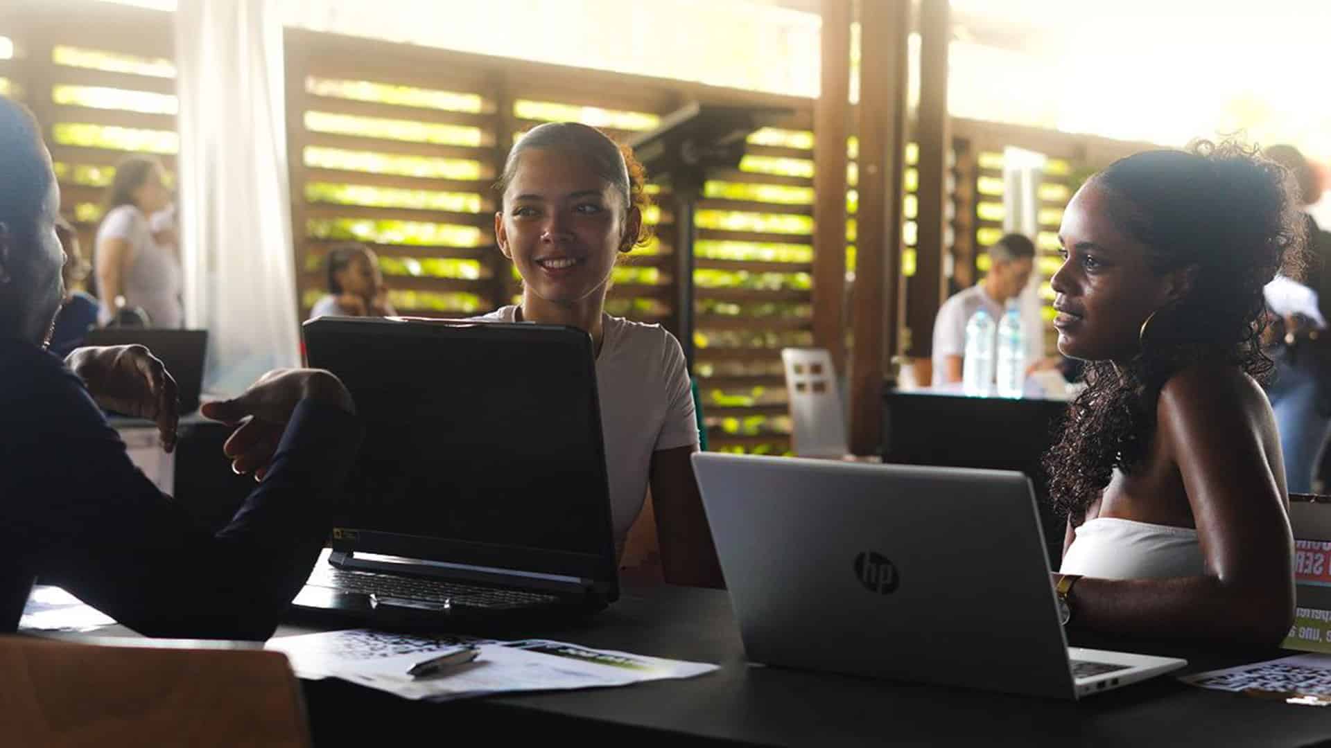 Trois jeunes adultes échangent avec des recruteurs lors du Job Dating de l’Université de Guyane 2025, assis autour d’une table avec leurs ordinateurs portables, dans une ambiance conviviale et professionnelle.