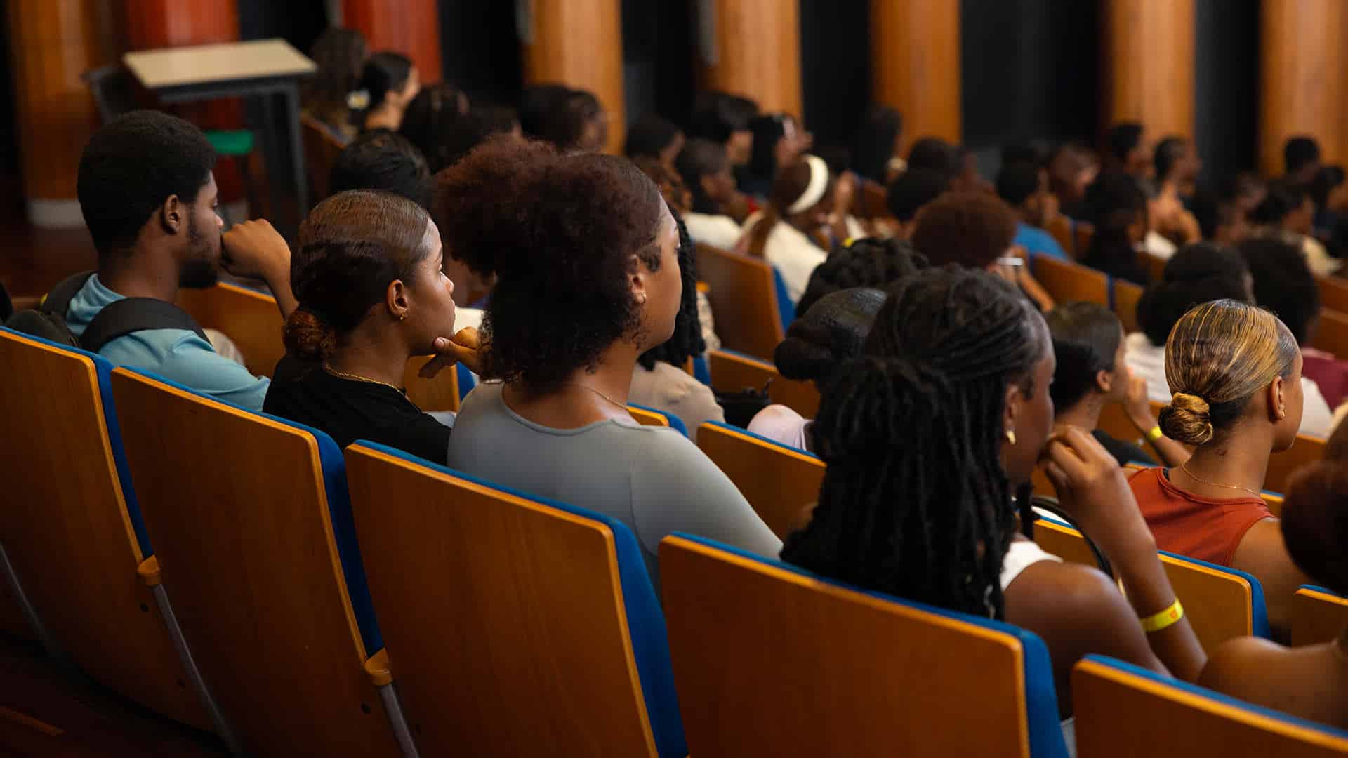 Étudiant·es et primo-arrivants assis dans un amphithéâtre, de dos, attentifs aux discours lors de la rentrée universitaire à l’Université de Guyane.
